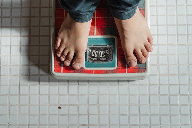Das Bild zeigt eine Gewichtswage, auf der eine eine Person steht. Das genaue Gewicht ist ablesbar.
